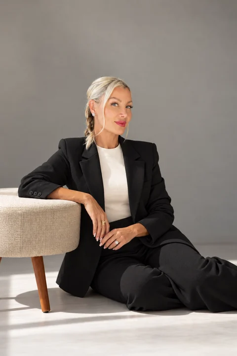 Amber Nicole Denney, founder of Euphoria Aesthetics & Laser, seated in a black suit beside a cream chair.